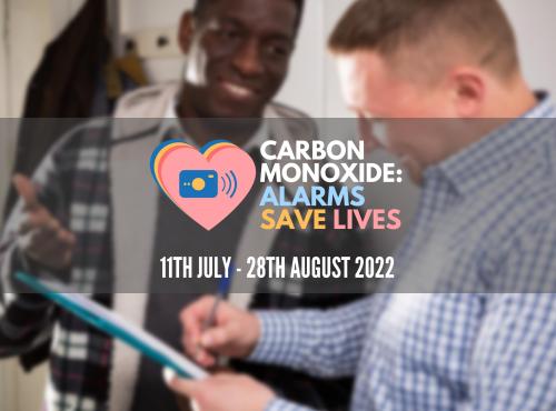 Two people looking at a clipboard. Reads: Carbon Monoxide: Alarms Save Lives 11 July - 28 August