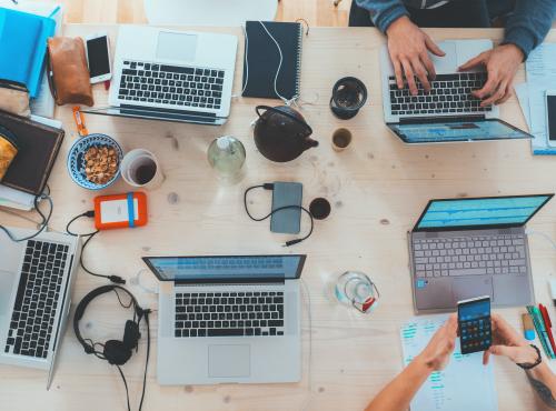 People working together by a desk. Overview of laptops, phones, food, coffee, while working.