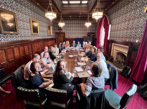 Overview of roundtable in House of Commons with attendees smiling into the camera.