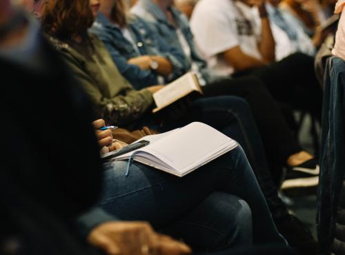 People sitting at a conference, taking notes on paper