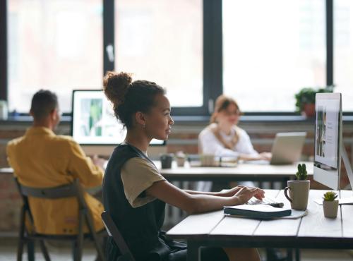 Picture of a girl on personal computer in the foreground, two people looking at their own computers in the background