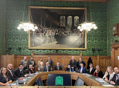 Commissioners and speaker sit around horse shoe table at Parliament looking into camera