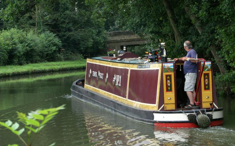 Photograph of a man steering a narrowboat in Northamptonshire | Photograph by David Merrett | Available under Attribution 2.0 Generic (CC BY 2.0) licence